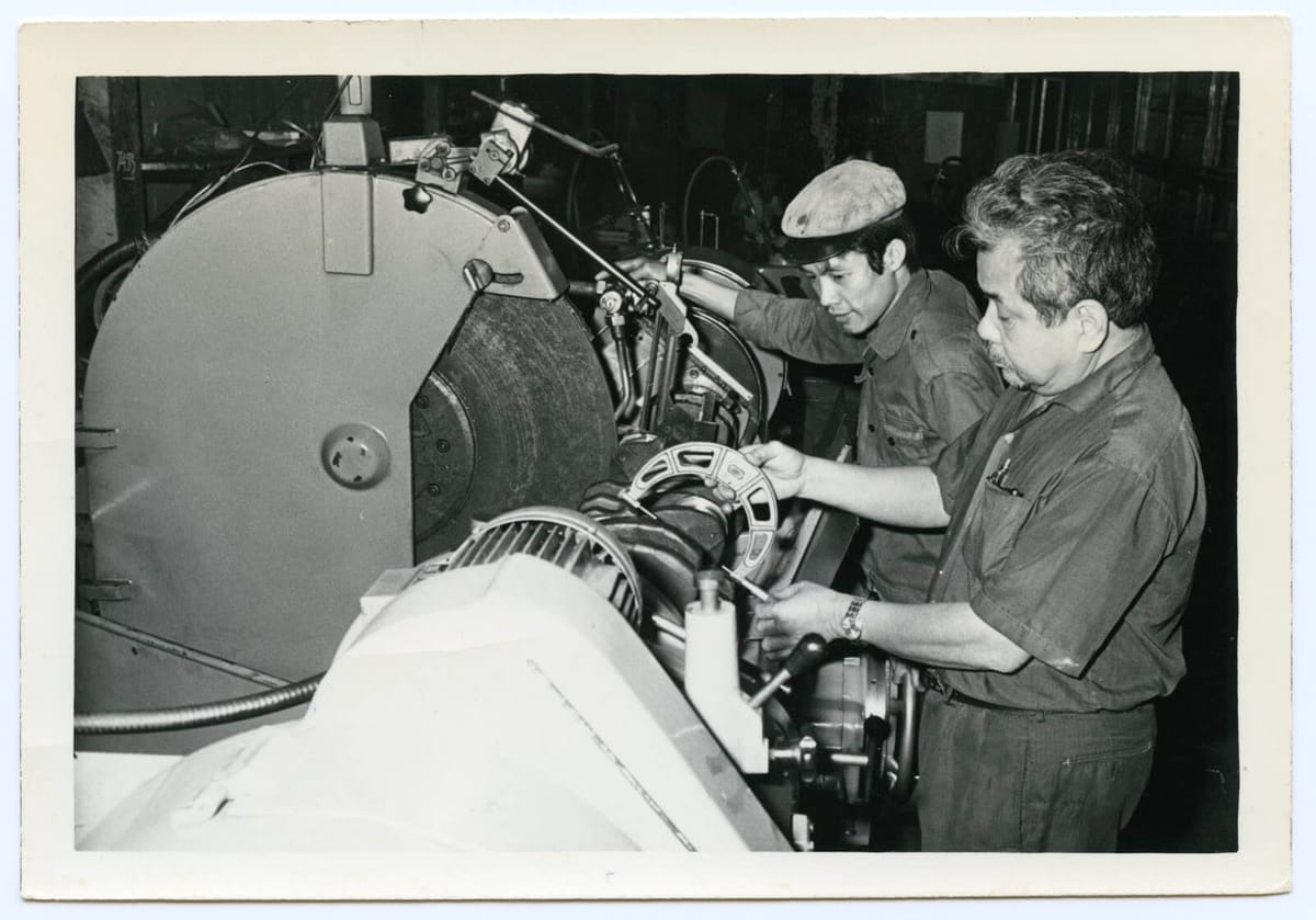 Two machinists at work on a lathe in a workshop, in a black-and-white print from the 1970s